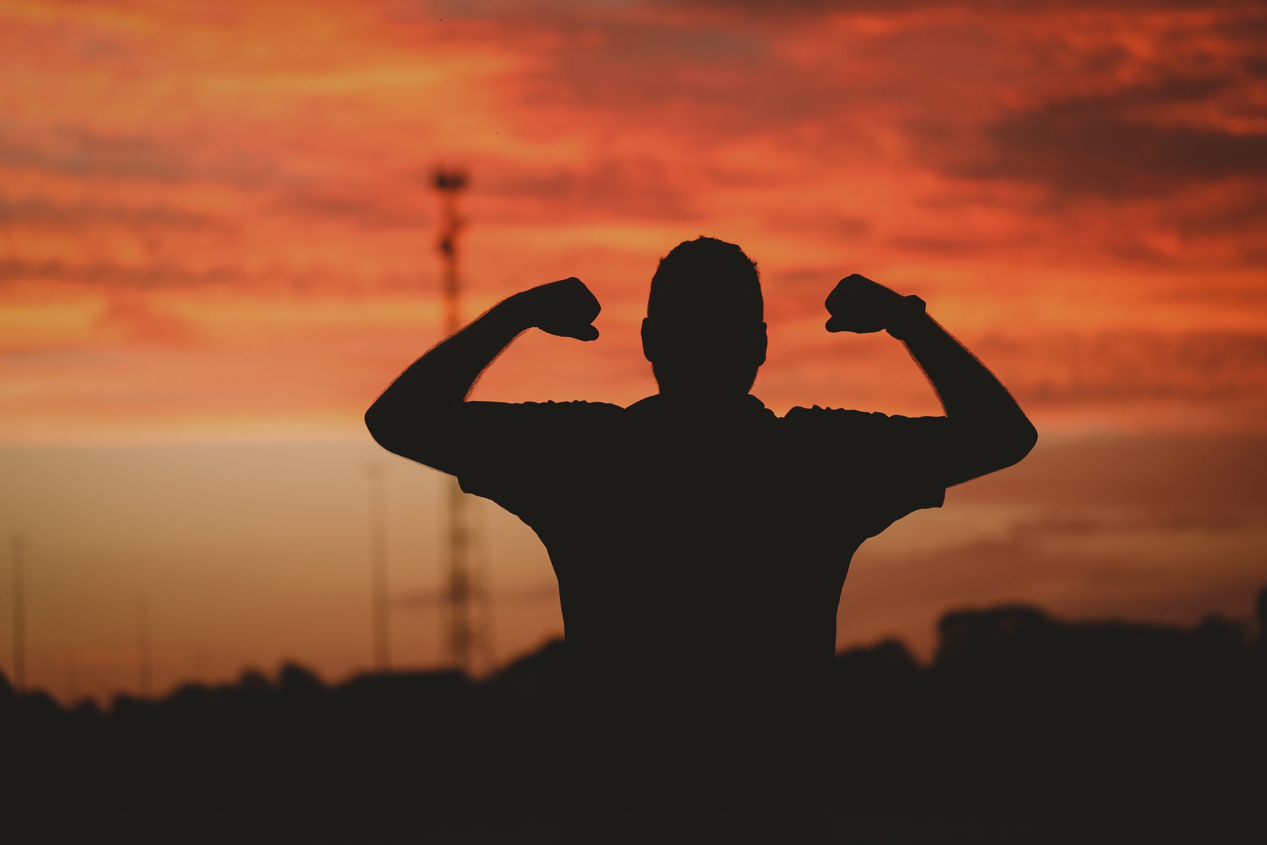 A silhouette of a strong man under a cloudy sky during the golden sunset