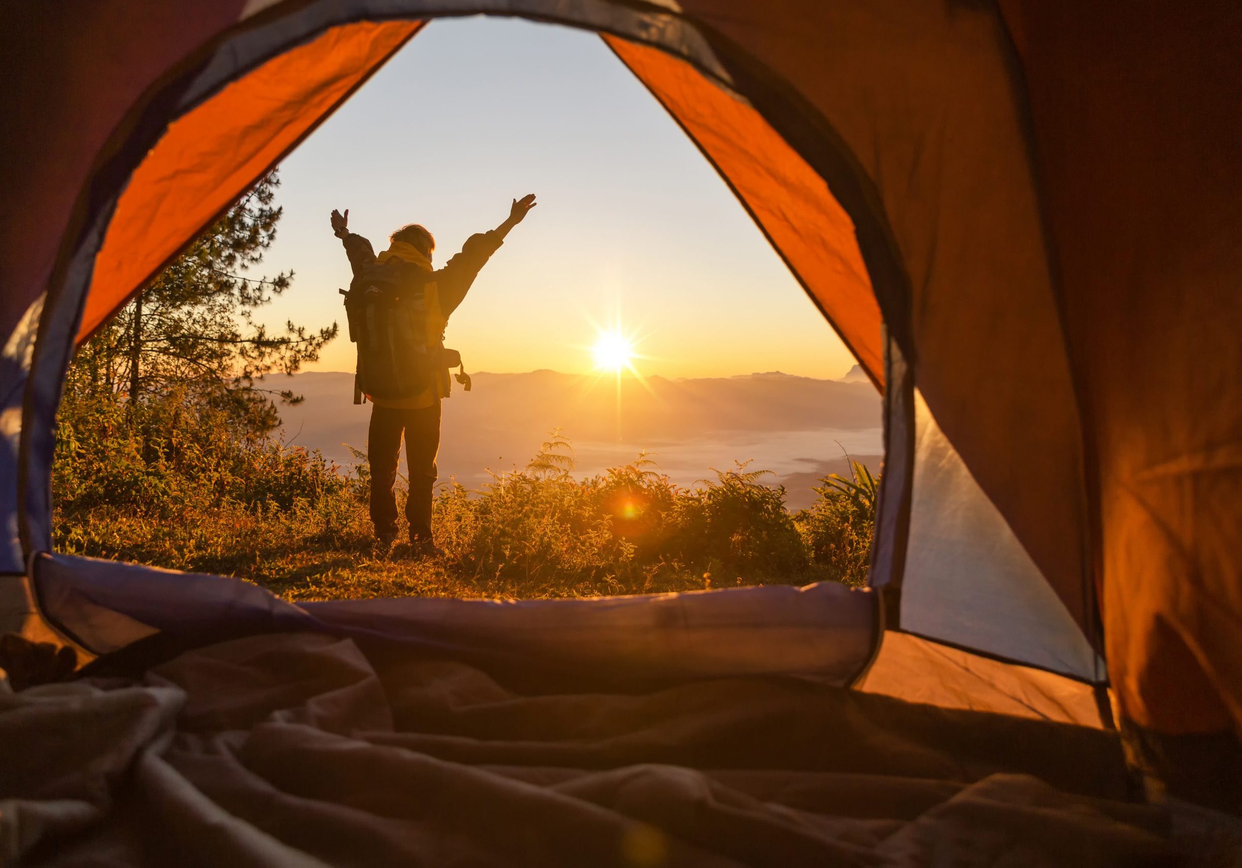 Hiker stand at the camping front orange tent and backpack in the mountains. Backpacker looking into the distance