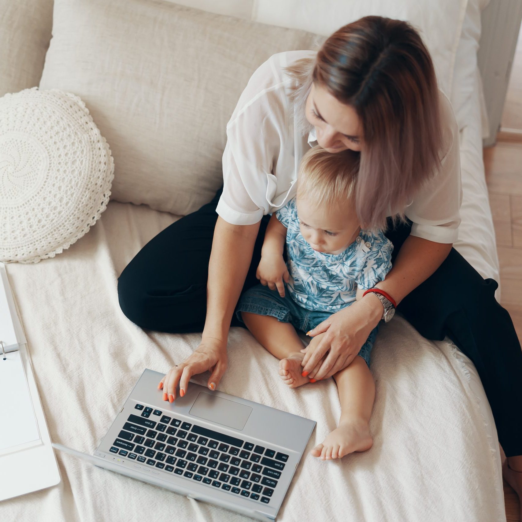 Young mother with her child working on laptop in bedroom at home. Multi-tasking, freelance and motherhood concept