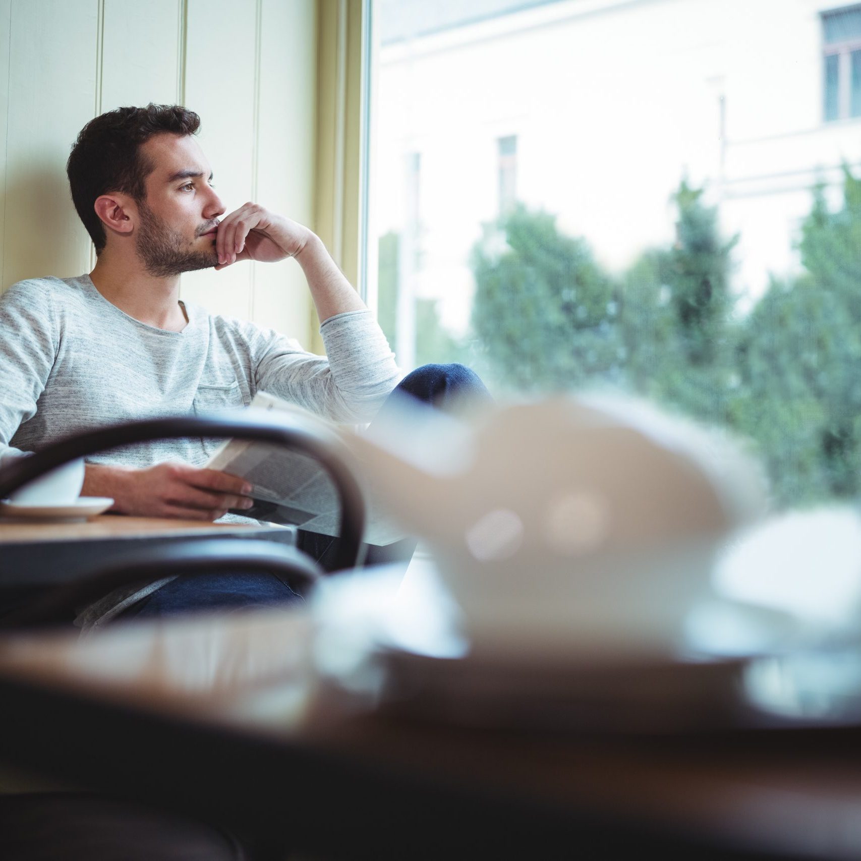 Thoughtful man looking through window while reading newspaper in cafÃ©